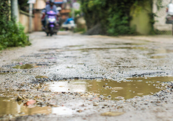 Rain falls in mud puddles in rough road, motorcycle blurred in background