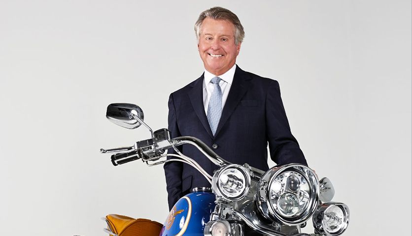 Karney Clayton attorney in navy suit posing with blue and cream custom Harley-Davidson motorcycle.