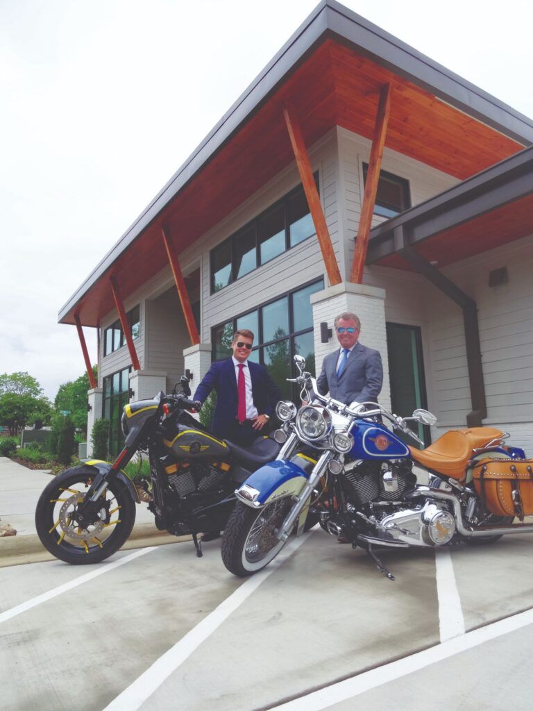 Two attorneys stand with motorcycles outside modern Karney Clayton office building