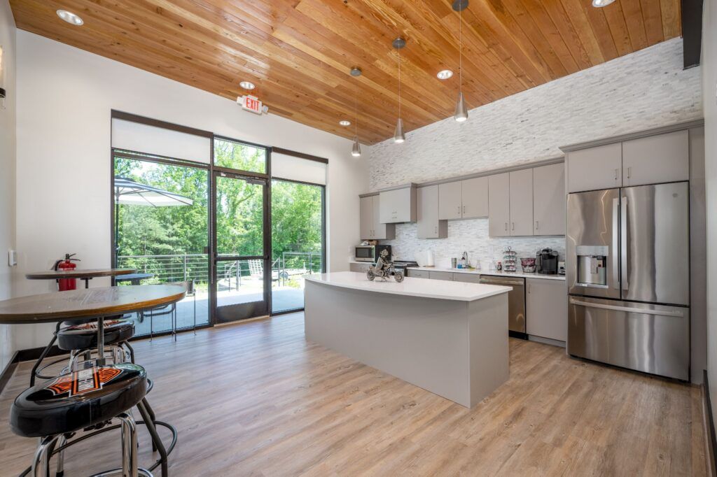 Modern kitchen with white island, gray cabinetry, wood ceiling, sliding glass doors to deck with forest views.
