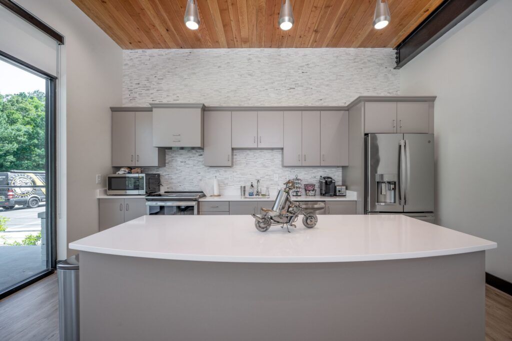 Modern kitchen with white quartz island, gray cabinetry, brick backsplash, stainless appliances, and wood ceiling.