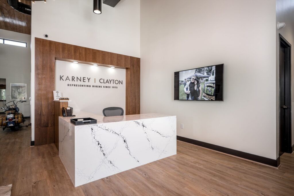 Karney | Clayton law office reception area with branded wood wall sign, white marble desk, and motorcycle imagery.