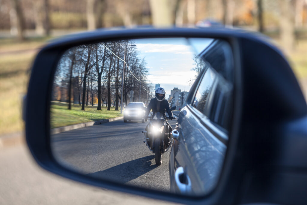 Motorcycle passing a vehicle seen in a side mirror, illustrating the risks of distracted and improper driving for motorcyclists in North Carolina