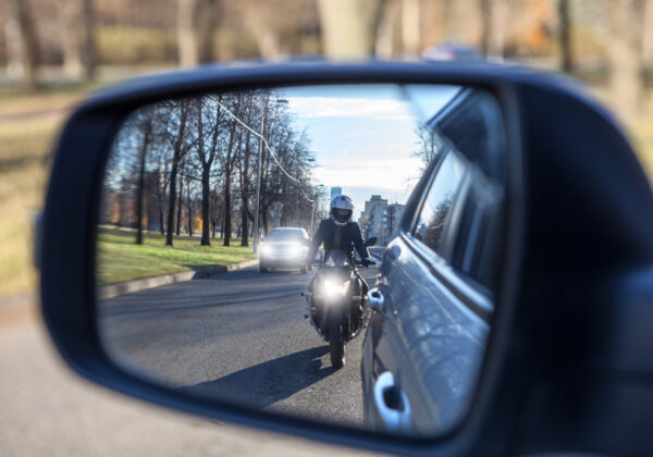 Motorcycle passing a vehicle seen in a side mirror, illustrating the risks of distracted and improper driving for motorcyclists in North Carolina