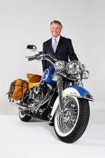 Karney Clayton attorney in navy suit posing with blue and cream custom Harley-Davidson motorcycle.